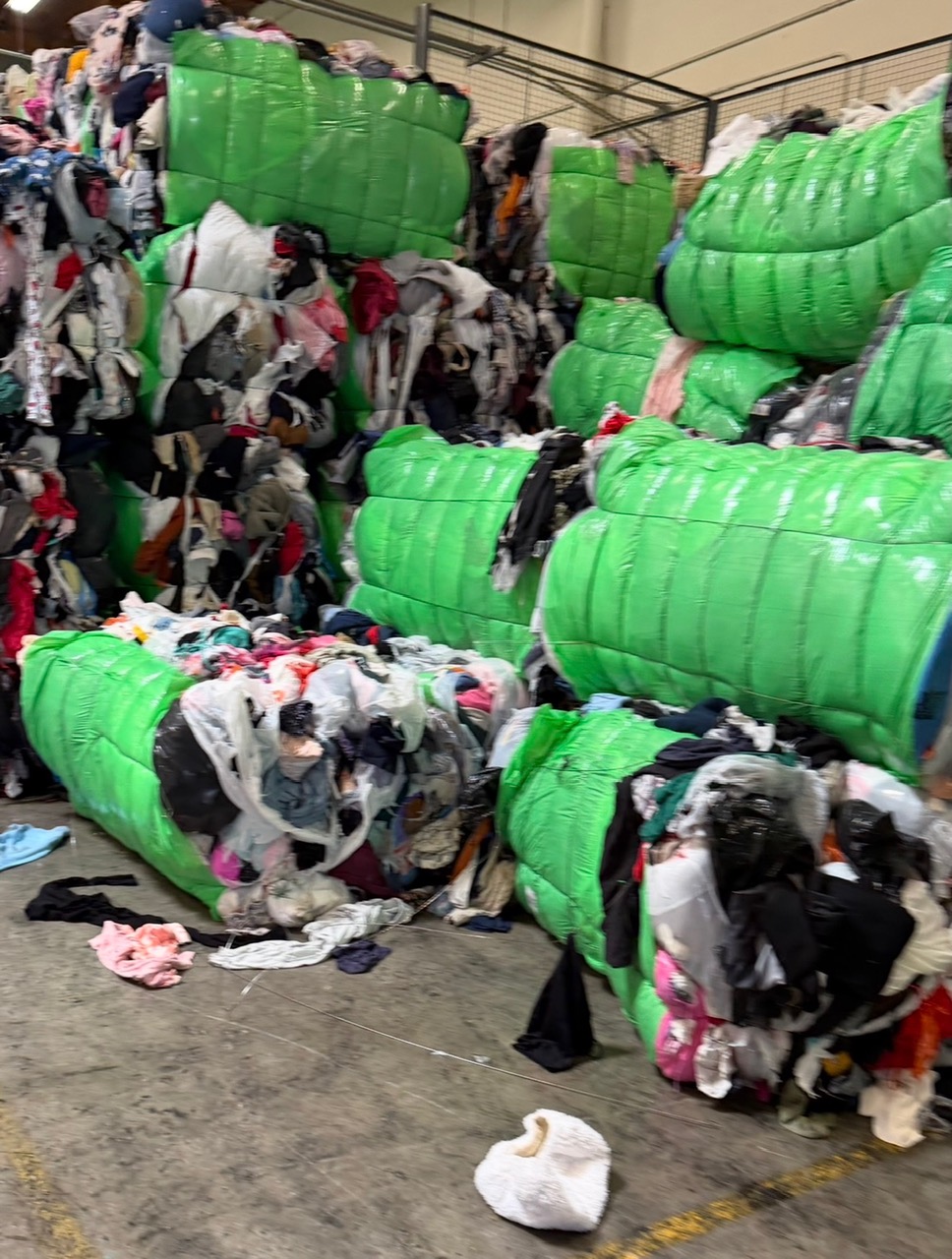 Green-wrapped bales of raw credential clothing stacked on a warehouse floor